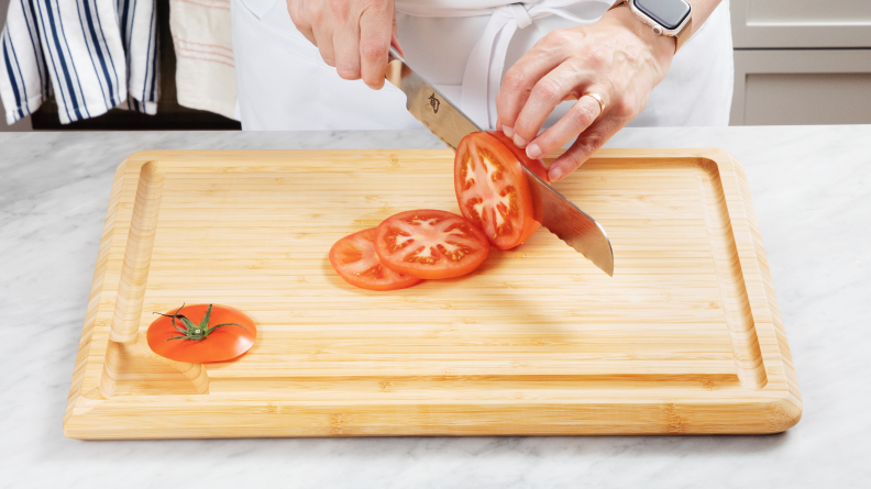 Person slicing tomato on bamboo cutting board
