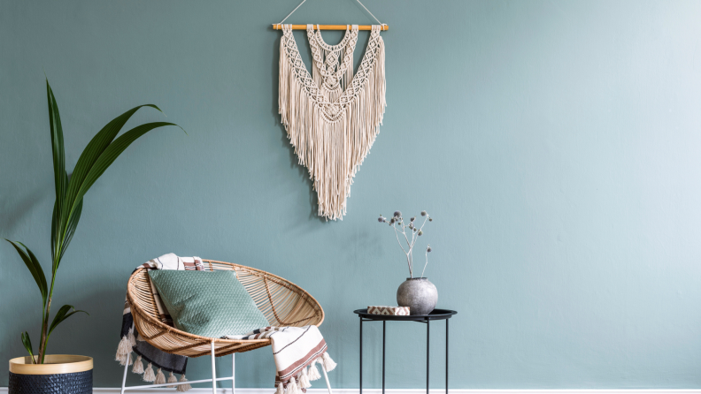 Macrame wall hanging accent on blue wall above accent chair and plant inside living room