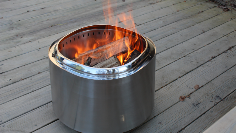 The East Oak fire pit on a wood deck with a fire burning inside and visible logs.