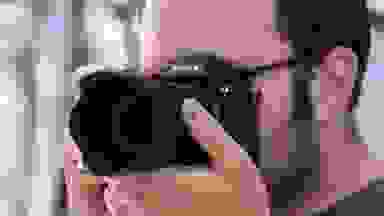 A photographer holds a camera viewfinder up to their eye to compose a shot.
