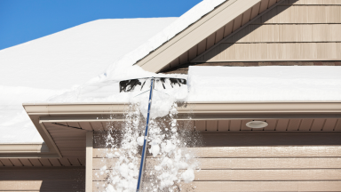 A person clears snow from their home with a roof rake.