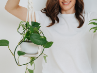 A person holds two house plants hanging from white macrame.