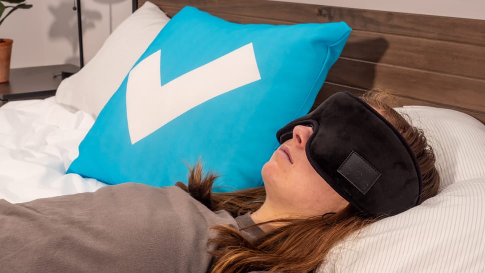 A person sleeps with a sleep mask on a bed.