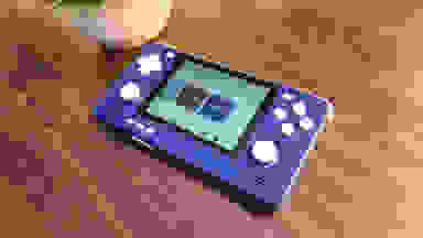 Blue Retroid Pocket 2S handheld game console on top of wooden surface next to potted plant.
