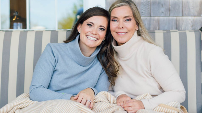 Two women founders of ChappyWrap on couch under ChappyWrap blanket