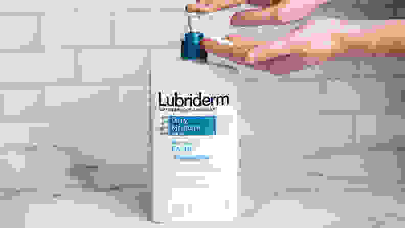 A person's hand pumping a white bottle of body lotion.