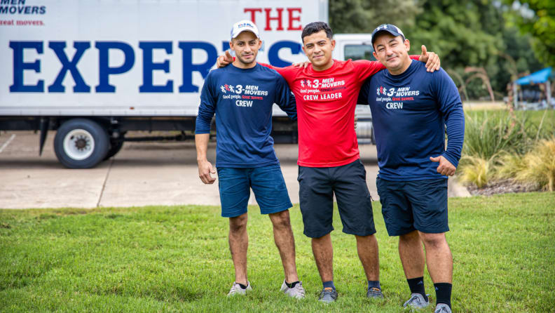 three men standing on a lawn in front of a moving truck