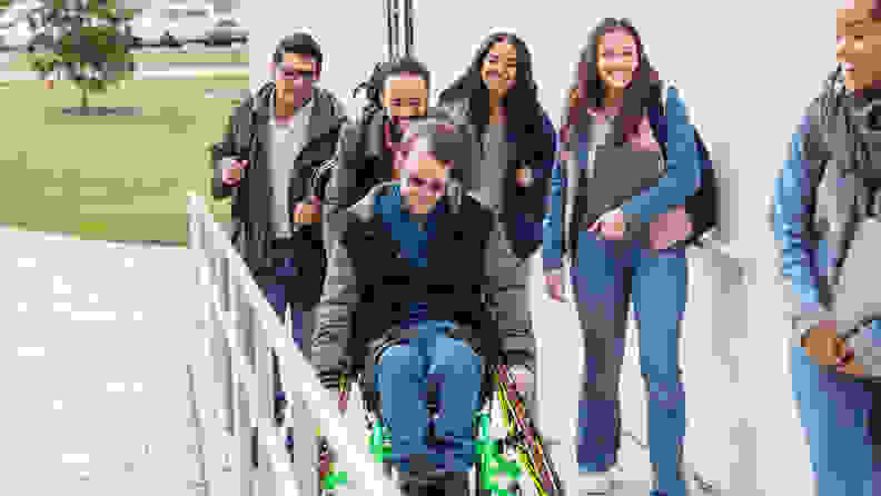 Smiling students traveling to class while pushing one student in a wheelchair.