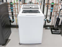 A solid white GE washer inside of the Reviewed testing labs in the middle of two other washing machine units.
