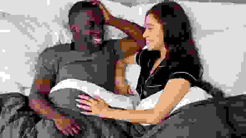 a man and woman in bed talking beneath a gray gravity blanket