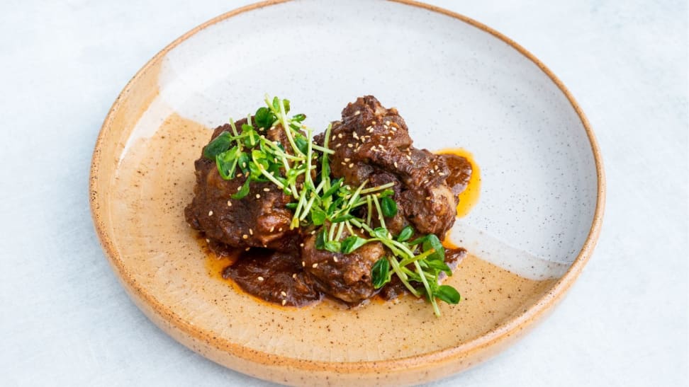 A white and orange plate filled with braised oxtail and topped with micro greens.