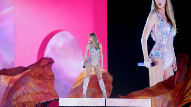 A photograph of Taylor Swift performing in concert, wearing a sparkly leotard and glitter boots.