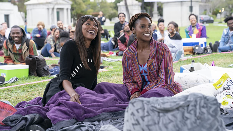 A still from the series Insecure featuring Issa Rae and Yvonne Orji sitting on a picnic blanket.