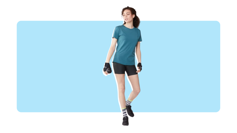 Model wearing black Pearl Izumi Sugar bike shorts with teal short-sleeved compression top and fingerless athletic gloves as she holds water bottle.