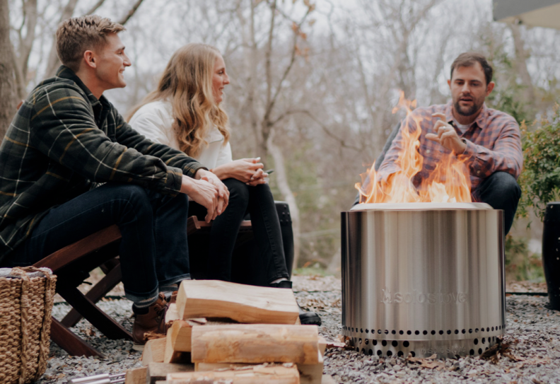 A group of people sitting around a Solo Stove in winter gear.