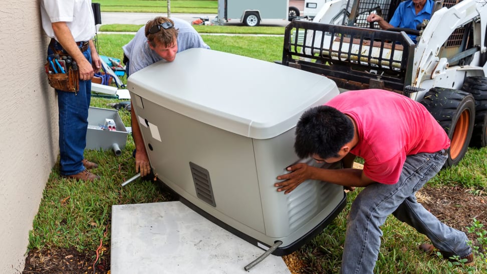 A group of men are moving a standby generator off of a fork lift and onto a platform set up in someone's yard.