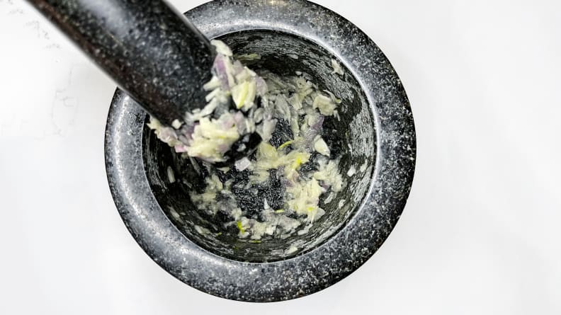 A person grinds alliums into a pulp using a mortar and pestle.