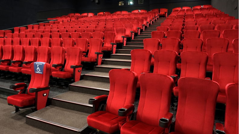 An auditorium filled with red chairs and on red chair with a handicap sign on it.