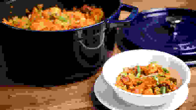 A pot full of jambalaya with the lid removed, next to a bowl full of the dish on a countertop.