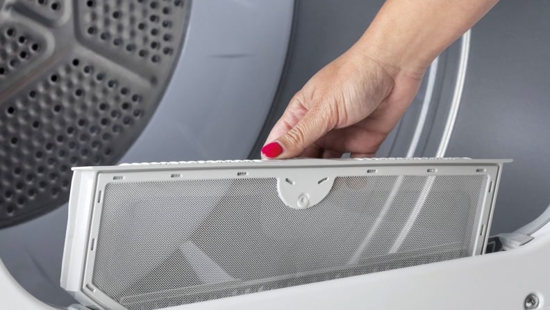 A hand reaches into frame, partially removing the GE GTD33EASKWW front-loading dryer's lint trap.