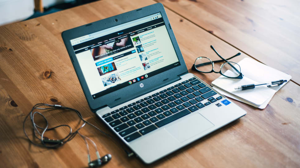 HP Chromebook sitting on a table next to glasses, a notebook, and some wires