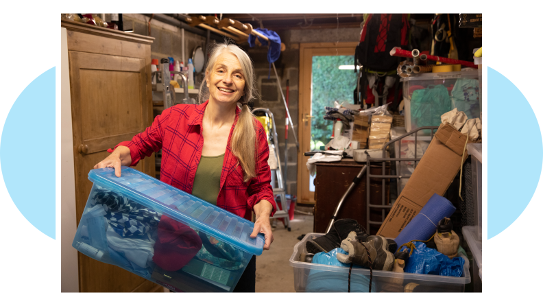 Senior citizen holding storage box while moving items in garage.