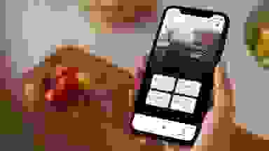 一只手拿着智能手机，放在一个烹饪板上，上面有一些切碎的蔬菜。手机屏幕上显示了惠而浦应用程序，用户正在查看惠而浦洗衣机的状态。