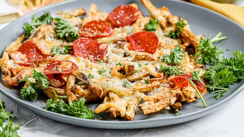 A gray plate of french fries topped with cheese, pepperoni, and parsley.