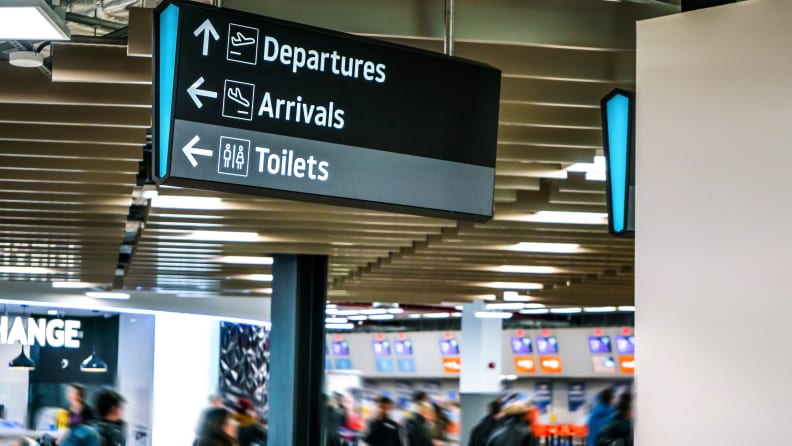 Blurred anonymous people walking under information table, under arrival, departure, and toilets sign at the airport.