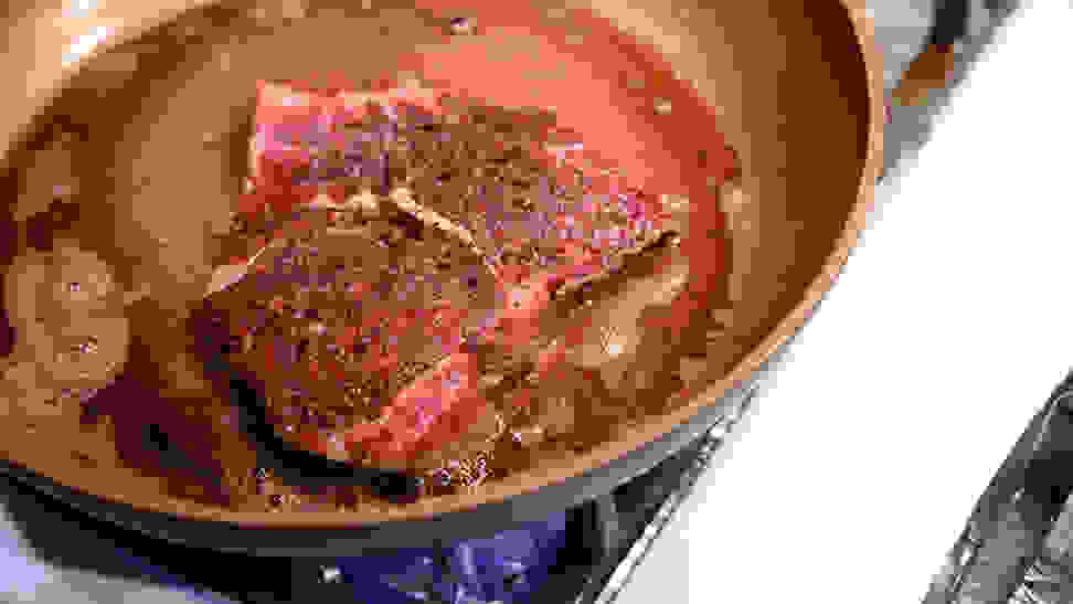 A bone-in steak cooks in a skillet filled with butter.
