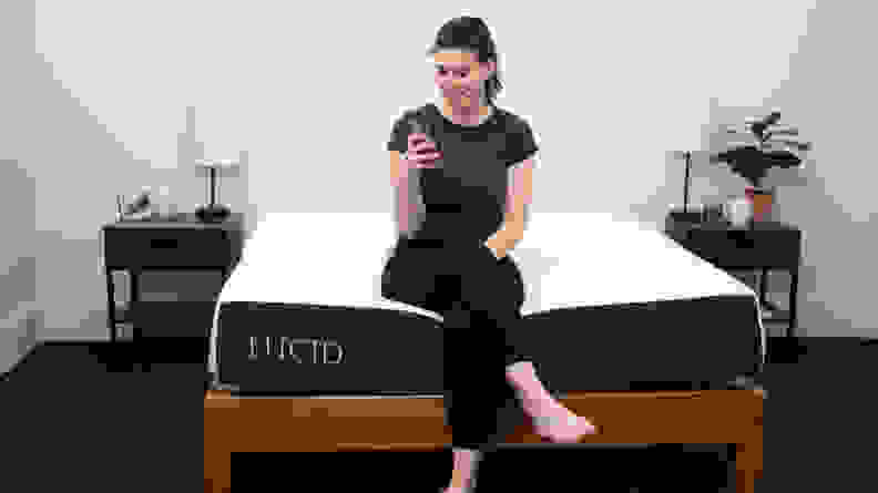 a person sits on the edge of the lucid mattress looking at their phone
