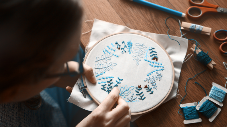 Person embroidering with blue color yarn on canvas material