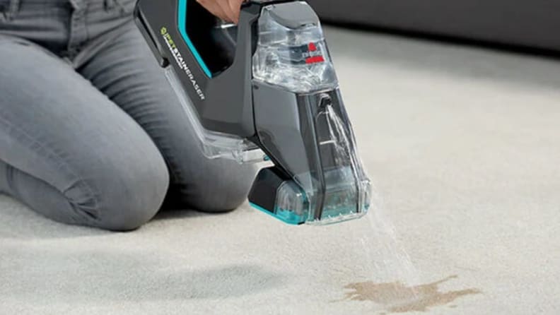 a person kneeling and using the bissell pet stain eraser on carpet