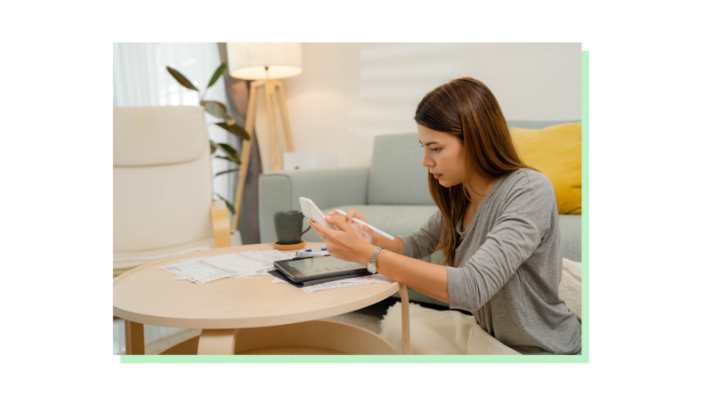 Person reviewing financial paperwork at coffee table on floor with calculator in hand.