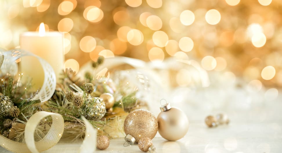 Gold Christmas ornaments surround white burning candle and Christmas lights.