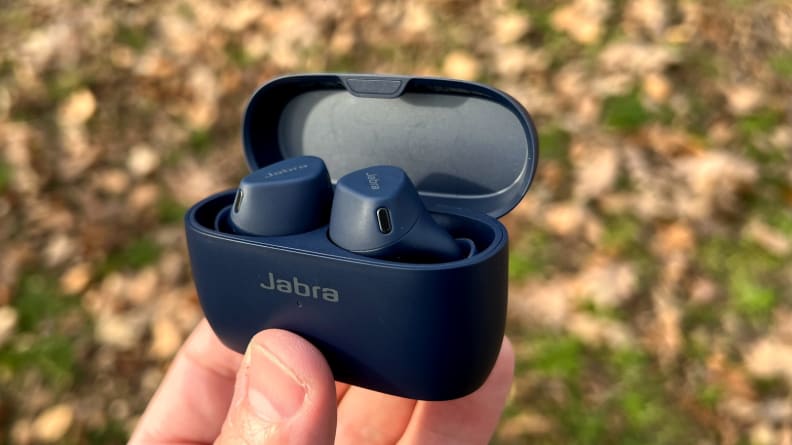 Jabra's navy Elite 4 Active headphones are held in their case above the yellow leaves.