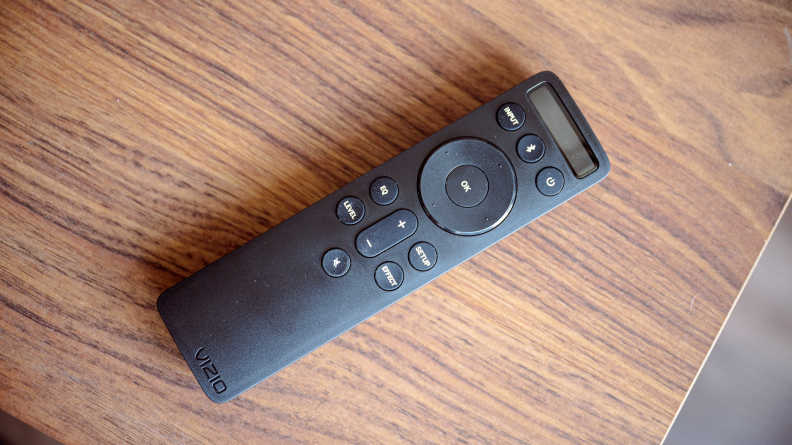 A black soundbar remote sits on a wooden console