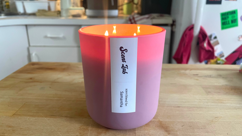 A pink Scent Lab candle on a wooden table with a personalized scent label on the candle.