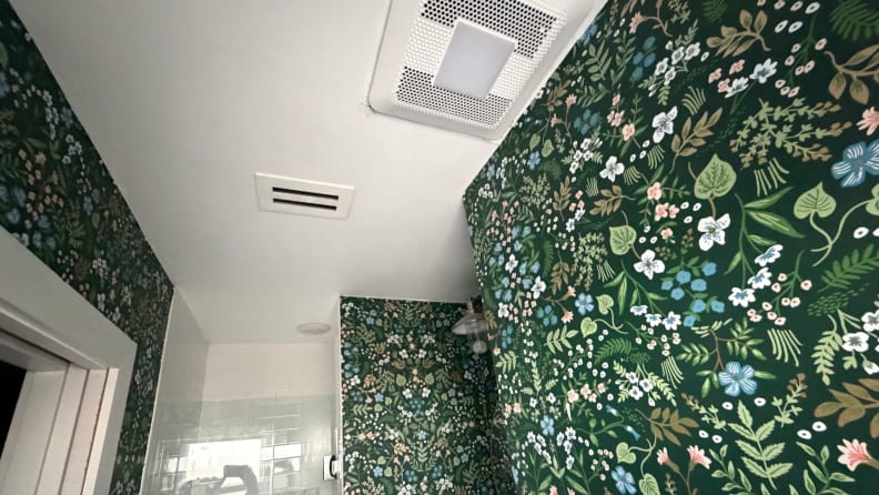 An exhaust fan on a ceiling next to a green floral wall