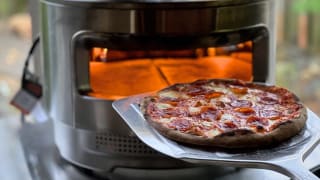Person using metal pizza peel to take small pepperoni pizza out of Solo Stove Pizza Oven.