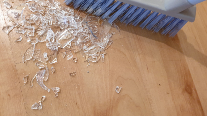 Broken glass on a hardwood floor being swept up by a blue-colored broom