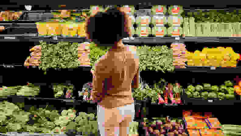 A woman looking at the produce shelf in a grocery store.