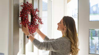 Person in gray sweater hanging berry wreath on door.