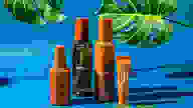 An assortment of tan Cay Skin bottles against a blue background and foliage.