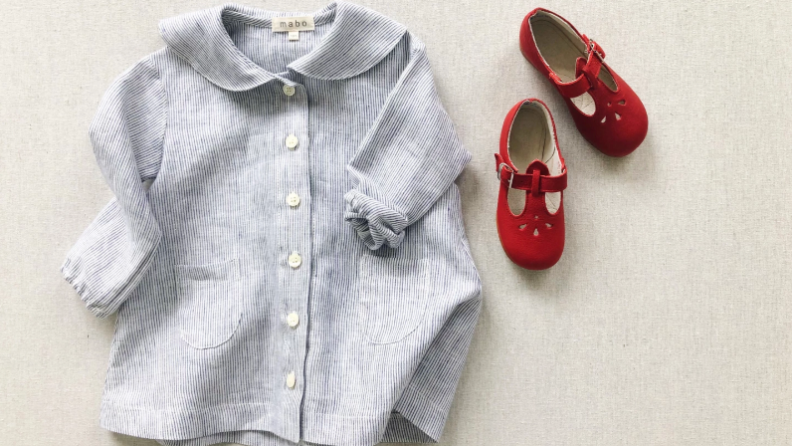 A girls' cotton dress and a pair of red t-strap shoes on a cream colored background