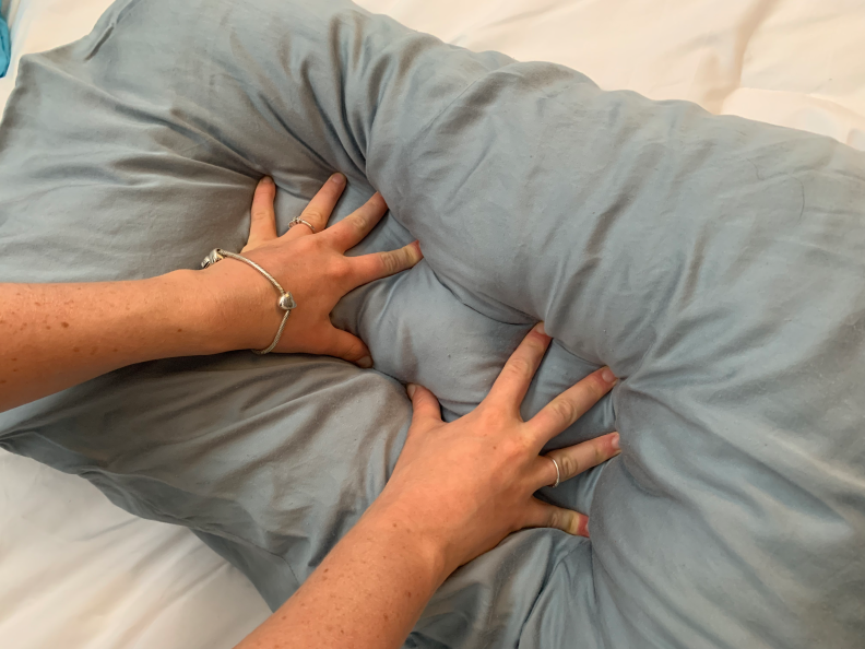 A blue pillow on a white bed. Two hands are pushing the pillow down, squishing it and the pillowcases.