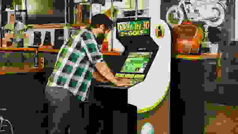 A person playing the Golden Tee 3D Golf arcade cabinet at a bar.