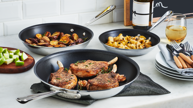 Three All-Clad nonstick frying pans filled with food sits on a kitchen counter.