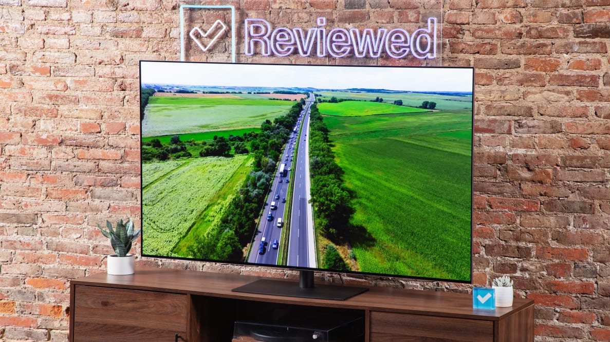 An LG G4 OLED TV on a wood entertainment center with a Reviewed sign above the TV.