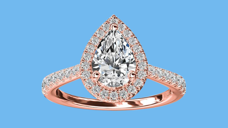 An image of a rose gold engagement ring with diamonds on the band, in a halo framing a pear-shaped diamond.